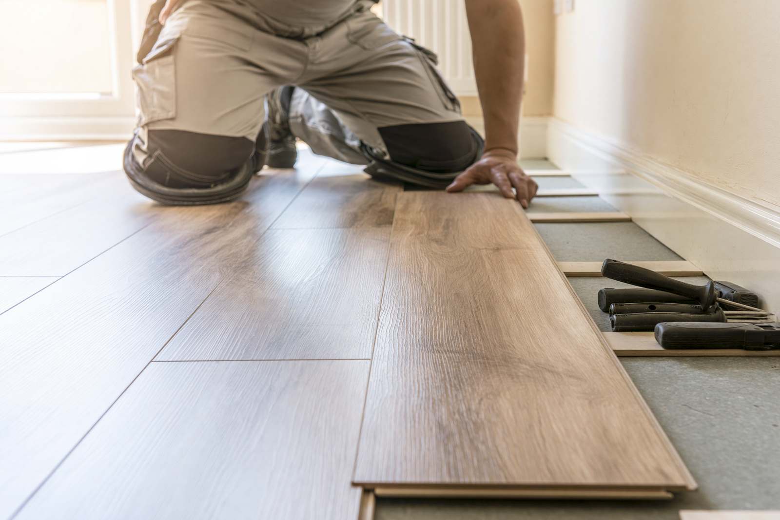 Wood-effect flooring planks being clicked into place during a fitting, with fitting tools alongside